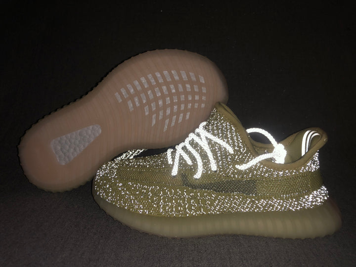 Pair of olive-yellow and black Yeezy 350 V2-style kids sneakers shown with the translucent outsole facing upward.
