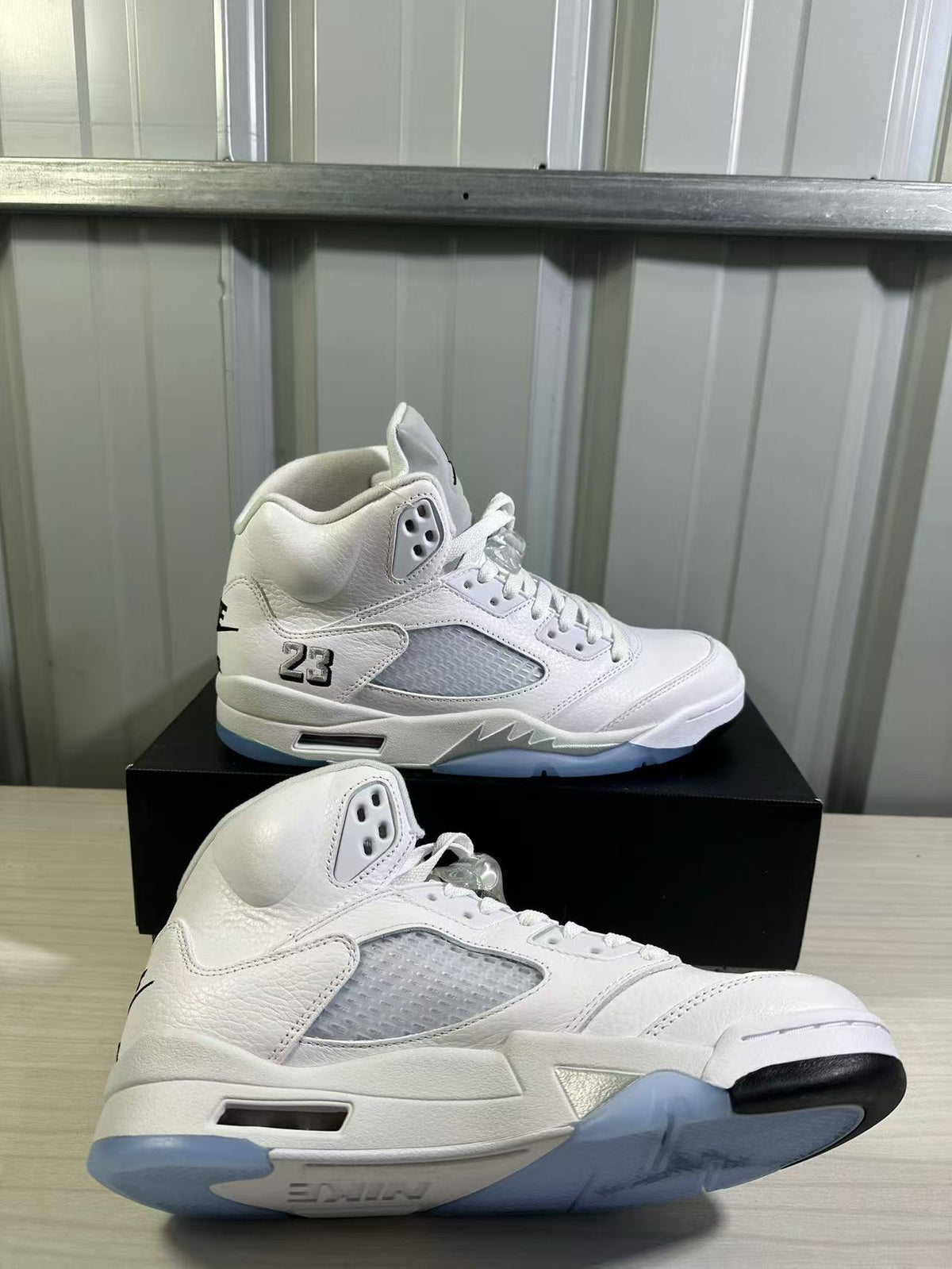 Pair of white and silver high-top sneakers shown from the side on a black shoe box.