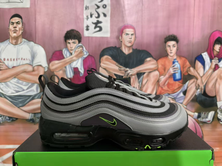 Side view of gray and black Nike sneakers with green Swoosh accents and layered wave panels, displayed on a green shoebox.
