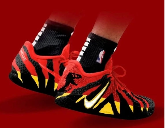 Red and black low-top sneakers with white swoosh branding, yellow accents, red laces and black textured panels shown against a red background.