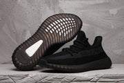 Black Yeezy 350 V2 sneakers shown together, with one shoe displaying the ribbed outsole and the other showing the side profile.