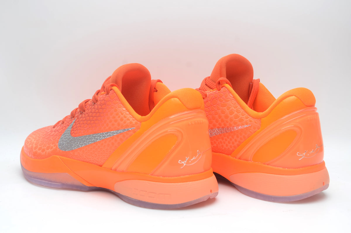 Pair of bright orange Nike basketball sneakers shown from the rear and side, with silver Swoosh details and translucent outsoles.