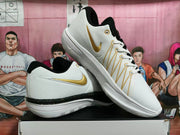 White basketball shoes shown at an angle, with gold Swoosh accents and black-and-gold midsole detailing.