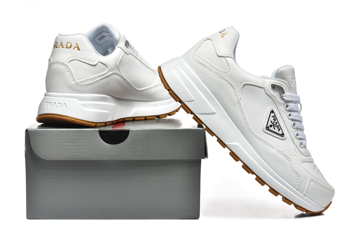 Pair of white Prada low-top sneakers with gum-colored outsoles, shown beside a shoe box.