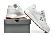 Pair of white Prada low-top sneakers with gum-colored outsoles, shown beside a shoe box.