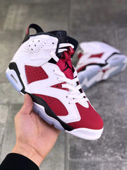 Front three-quarter view showing the red toe box, white overlays, red tongue, and black Jumpman logo.