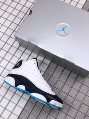 Air Jordan 13 sneaker beside a light-colored shoebox, showing the white perforated upper, black midsole, and blue outsole accent.