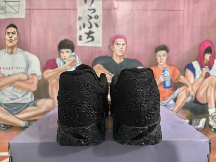 Rear view of black sneakers showing textured uppers and rugged black outsoles on a box.