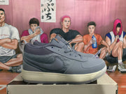 Side view of a gray Nike sneaker showing the Swoosh, textured side panel, layered upper, and off-white midsole.
