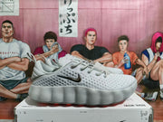 Side profile of a gray Nike sneaker showing the perforated upper, dark Swoosh, raised sole, and red outsole accents.