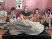 Side view of a white and gray Nike Zoom basketball sneaker showing the textured upper, gray swoosh, heel structure, and visible midsole branding.