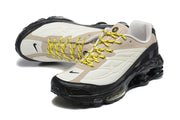 Angled view of Nike Shox Ride 2 sneakers showing the beige and cream upper, black overlays and yellow laces.