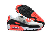 Side view of grey, black, white, and bright crimson Nike Air Max 90 sneakers with one shoe showing the outsole.