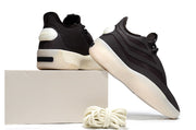 Black sneakers shown from the rear and side on a light box, highlighting the heel details and cream outsoles.