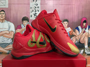 Angled view of two red Nike basketball sneakers showing the gold-and-black side graphic, black Swoosh, gold toe accent, and layered outsole.