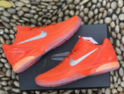 Pair of orange sneakers displayed on a black box from an angled top view.