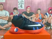 Side view of a navy and black basketball shoe with blue accents, a white Swoosh, and coral-red outsole.