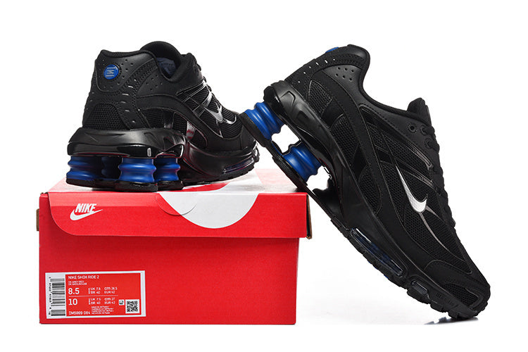 Black Nike Shox R4 sneakers with blue sole accents displayed on a red shoe box; the box label shows a sample size.