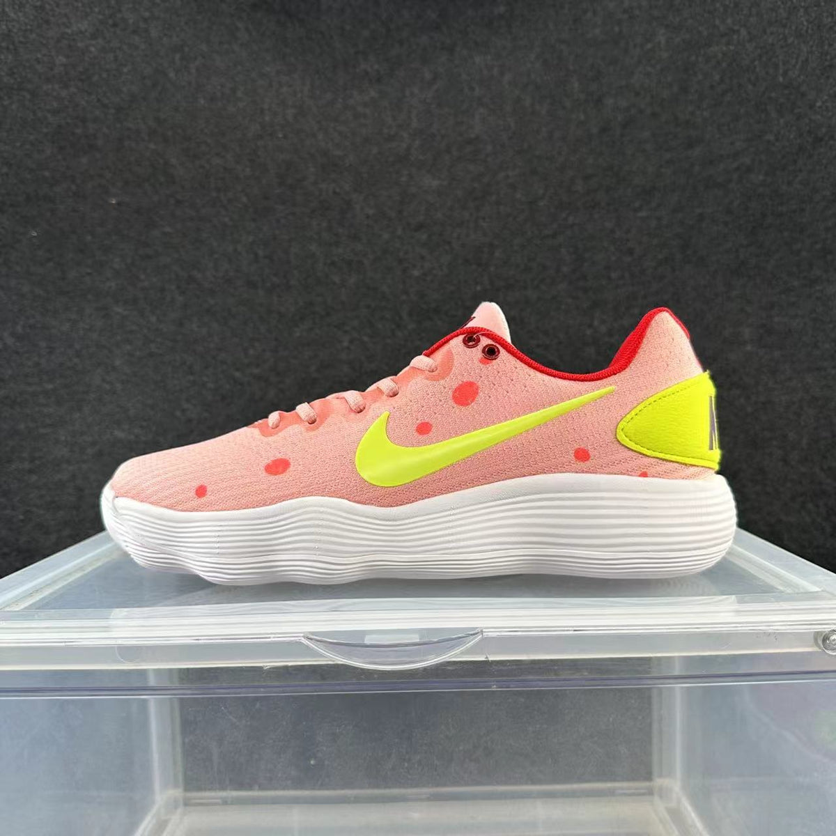 Side view of a pink low-top Nike sneaker with red dot accents, a bright yellow Swoosh and heel panel, and a white ridged sole