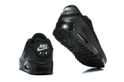Black Nike Air Max 90 sneakers shown from the heel, with one shoe turned to reveal the outsole.