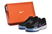 The sneaker pair displayed beside an orange Nike shoe box, showing the black, blue, purple, and white color scheme.