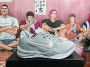 Side view of a grey Nike basketball sneaker with a white swoosh, lace-up upper, sculpted midsole, and visible heel signature-style detail.