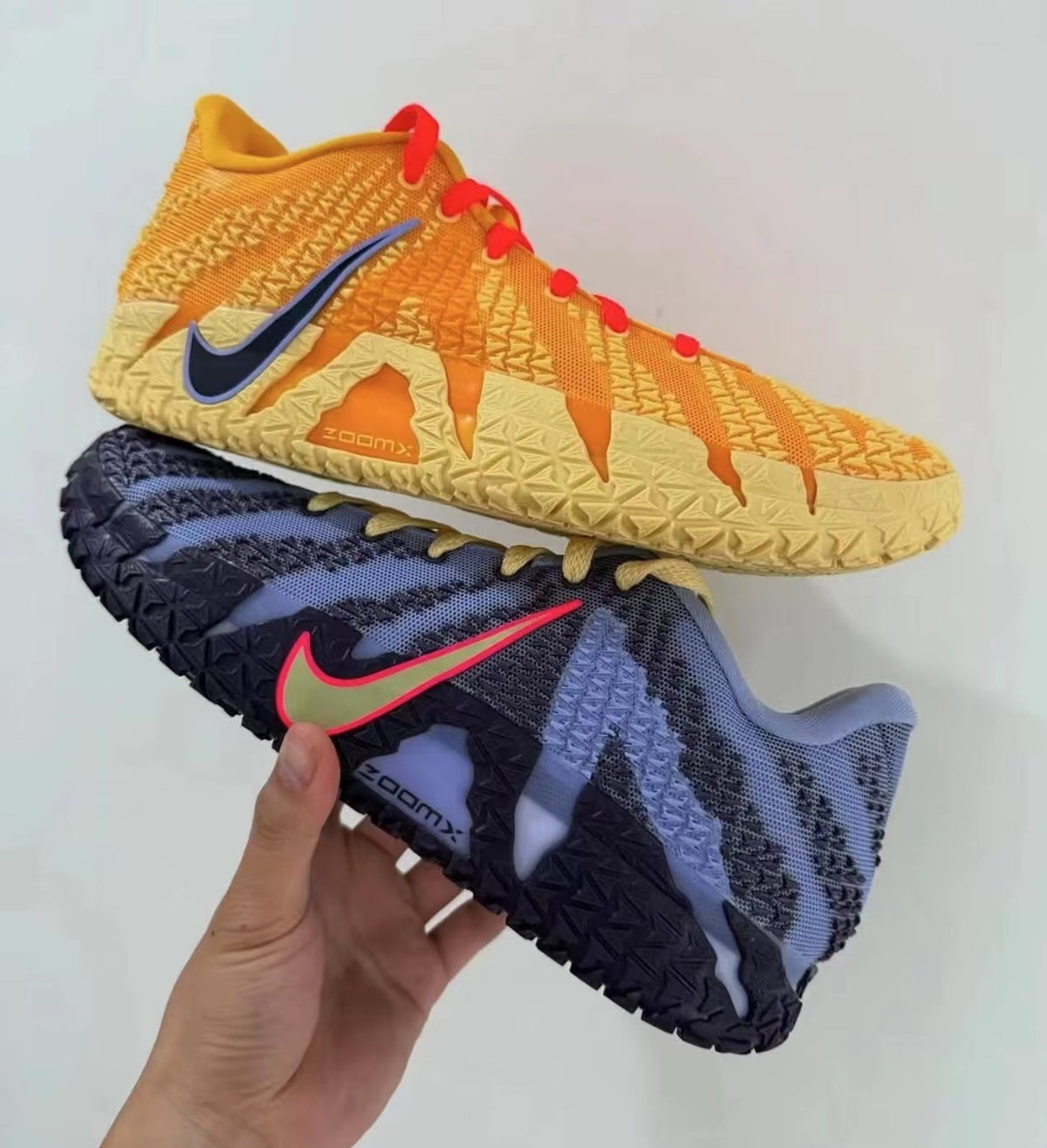 Pair of Nike sneakers shown in mismatched orange and cream and dark blue and black colorways, with contrasting Swoosh logos, red accents, textured uppers, and ZoomX lettering.
