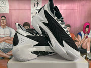 Pair of black-and-white basketball sneakers displayed on a shoebox, showing the layered side panels, patterned laces, and sculpted sole.