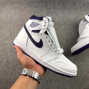 Handheld angled view of a single white and purple Jordan high-top sneaker showing its side profile and perforated toe box.
