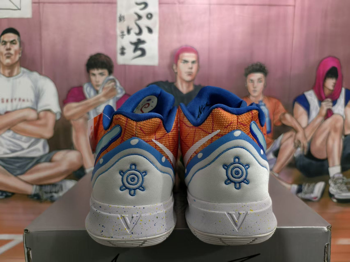 Rear view of orange, blue and white basketball sneakers with circular embroidered heel details, displayed on a shoebox.