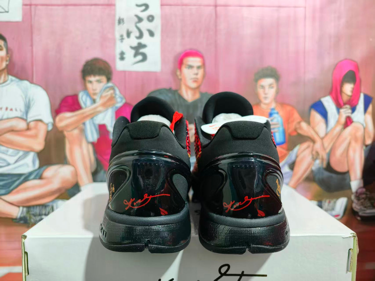 Rear view of black basketball sneakers with glossy heel panels, red accents, and gold detailing, displayed on a shoebox.