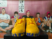 Front view of yellow-gold basketball sneakers with purple-accented outsoles and perforated toe boxes.