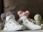 Pair of white high-top sneakers shown from the front with ankle straps and graphic upper details.