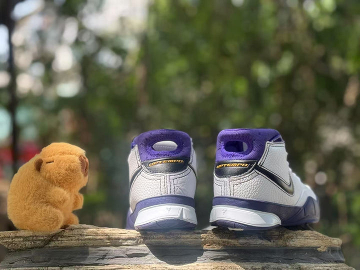Rear view of white and purple high-top sneakers with Kobe and UPTEMPO-style heel details beside a teddy bear