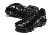 Close three-quarter view of a black Nike Air Max Plus sneaker with glossy overlays and a silver Swoosh.