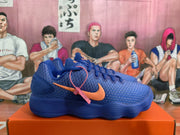 Side view of a blue Nike sneaker with orange branding, textured upper, padded heel, and ribbed outsole.