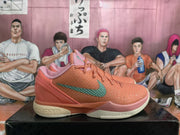 Side profile of a coral-orange basketball sneaker showing the textured upper, green Swoosh, pink heel accents, and cream outsole.