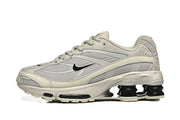 Side view of a cream and grey Nike Shox Ride 2 sneaker with mesh panels and black sole columns.