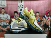 Angled view of the shoes showing yellow mesh-style panels, white overlays, and blue-patterned soles.