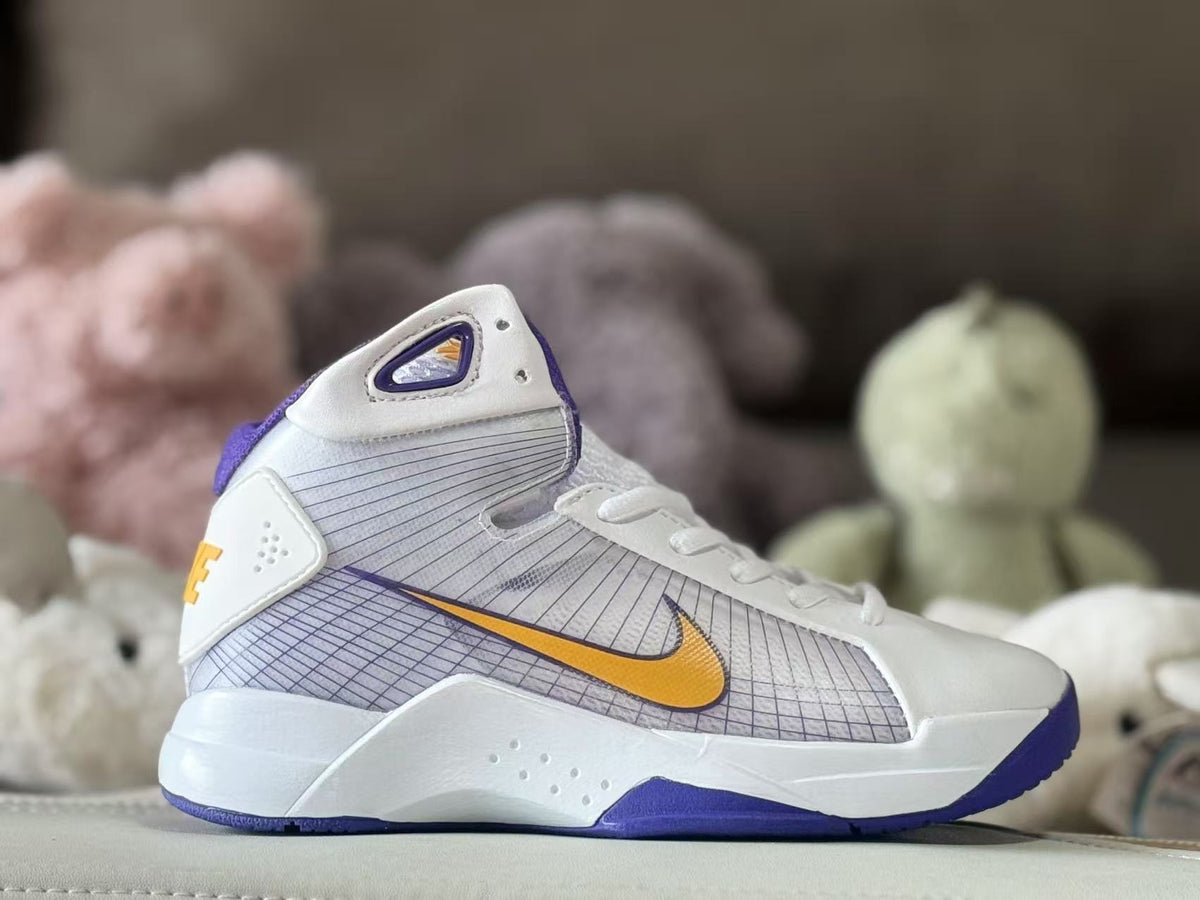 Side view of a white Nike kids’ high-top sneaker with purple trim, a gold Swoosh, and a patterned side panel.