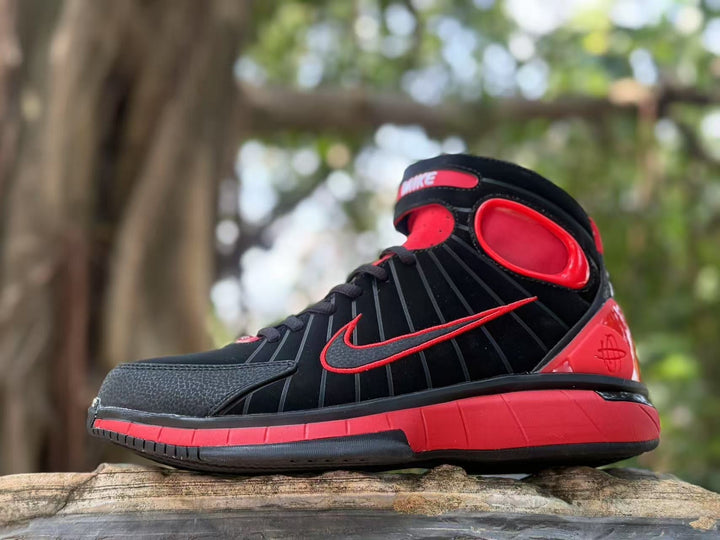 Side view of black and red 2K4 high-top sneakers displayed outdoors.