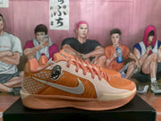 Side profile of an orange Nike sneaker with a silver Swoosh, light side panel, pink laces, and layered peach-colored sole.