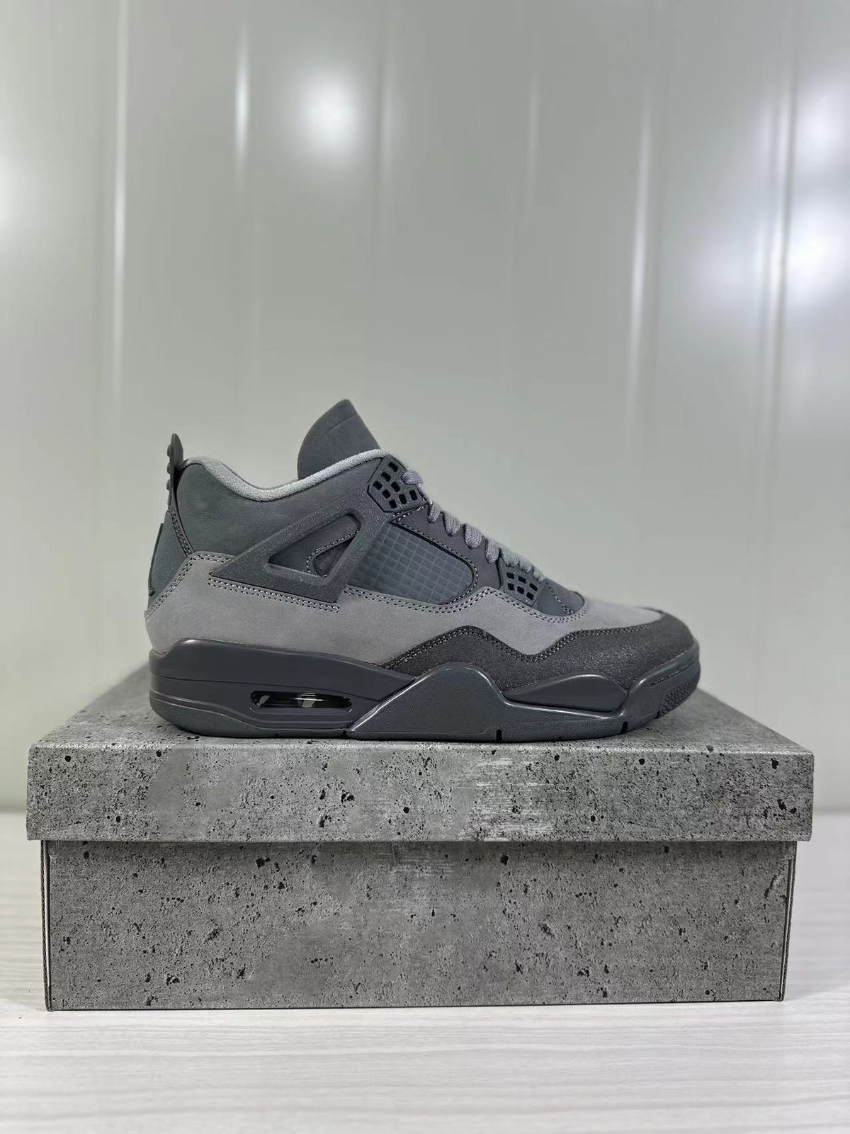Side profile of a grey and charcoal Air Jordan 4 Retro SE sneaker displayed on a textured grey box.