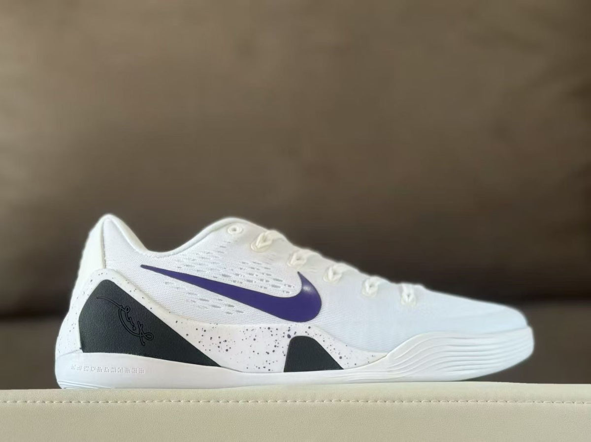 Side view of white Nike Kobe 9 sneakers with a purple Swoosh, black heel panel and speckled side detailing.