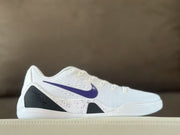 Side view of white Nike Kobe 9 sneakers with a purple Swoosh, black heel panel and speckled side detailing.