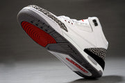 Underside view of a white and black Air Jordan 3 sneaker showing the gray and red outsole and elephant-print heel detail.