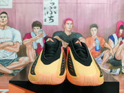 Front view of black basketball shoes with pale gold-toned panels and coral accents.