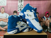 Angled view of a pair of white and blue Nike high-top sneakers with contrasting panels and ankle straps.