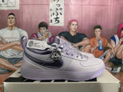 Side view of one purple and light gray Nike sneaker showing the dark Swoosh, padded collar, and attached hangtags.