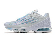Side profile of a white Nike Air Max Plus sneaker with blue detailing and visible cushioning.